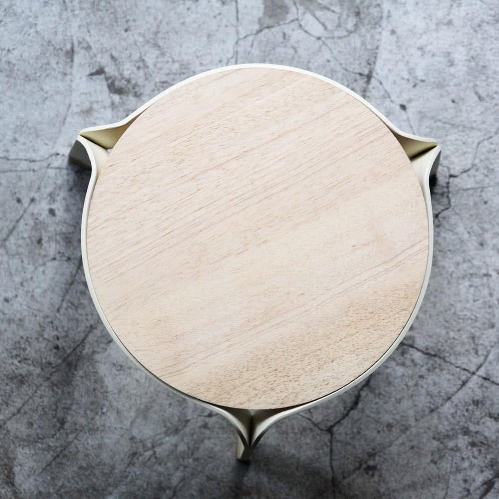 Top view of a round wooden stool with uniquely designed legs on a textured concrete floor