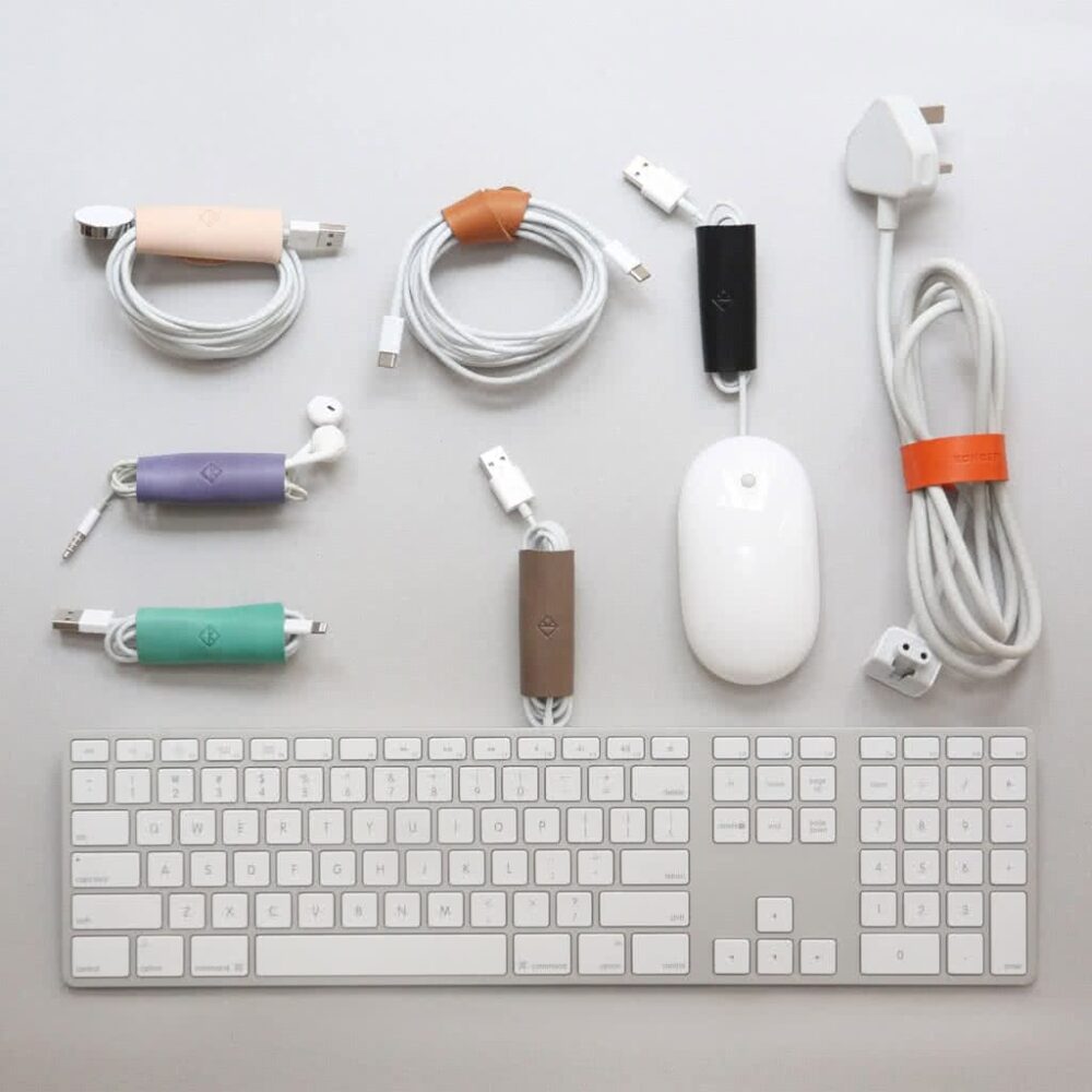 Various cables and a white computer mouse organized with colorful cable management clips, arranged around a white keyboard